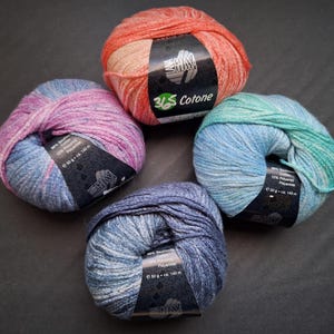May include: Four colorful balls of yarn in shades of pink, blue, orange, and teal. Each ball has a label that reads "365 Cotone" and includes the weight and length of the yarn. The yarn is a blend of cotton and polyamide.
