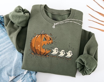 May include: Olive green sweatshirt featuring a Halloween-themed graphic. The design includes a carved orange pumpkin with a large mouth and three white ghost figures. A silver necklace is draped on the sweatshirt.