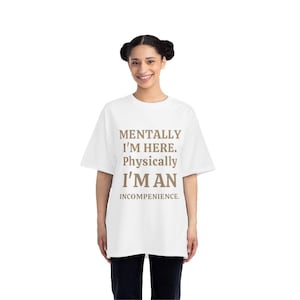 Puede incluir: Camiseta blanca con el texto "MENTALLY I'M HERE. Physically I'M AN INCOMPETENCE." en fuente marrón. La camiseta es de corte holgado y la lleva una persona. La persona lleva pantalones negros.