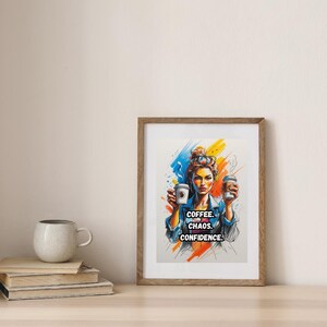 Könnte beinhalten: Gerahmter Kunstdruck mit einer farbenfrohen Illustration einer Frau, die zwei Kaffeetassen hält. Der Druck enthält den Text "COFFEE. CHAOS. CONFIDENCE." in fetter Schrift. Das Kunstwerk befindet sich in einem Holzrahmen und wird auf einer Holzoberfläche präsentiert.