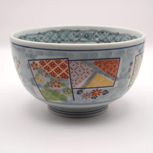 May include: A decorative ceramic bowl with a light blue base and patterned rim. The bowl has colourful geometric designs in red, yellow, and purple. Floral motifs are also present. Suitable for serving food.