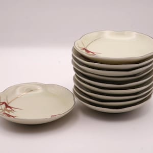 以下が含まれることがあります： 銀色の縁と赤と金の竹のデザインが施された、オフホワイトのスカラップエッジのプレートのスタック。 1つのプレートは別々です。 プレートは、前菜や小さな料理を提供するのに適しています。