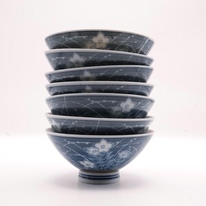 May include: A stack of six blue and white ceramic bowls. Each bowl features a floral design and a striped pattern. The bowls are stacked on top of each other, with the bottom bowl resting on a small, round base.