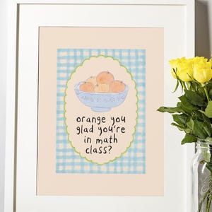 May include: Framed art print featuring a watercolor illustration of oranges in a blue bowl. The text "orange you glad you're in math class?" is written below the bowl. The print is in a white frame.