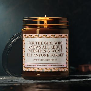 Könnte beinhalten: Eine brennende Sojakerze in einem braunen Glas mit schwarzem Deckel. Auf dem Etikett steht "FOR THE GIRL WHO KNOWS ALL ABOUT WEBSITES & WON'T LET ANYONE FORGET." Die Kerze hat eine Brenndauer von 50-60 Stunden.