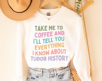 May include: White sweatshirt with the text "TAKE ME TO COFFEE AND I'LL TELL YOU EVERYTHING I KNOW ABOUT TUDOR HISTORY" in colorful letters.