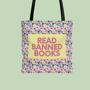Puede incluir: Una bolsa de tela floral con fondo amarillo y el texto "READ BANNED BOOKS" en letras rosas.