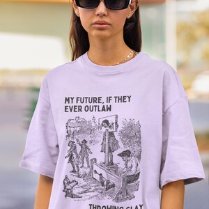 May include: A light purple t-shirt with the text "MY FUTURE, IF THEY EVER OUTLAW" above a black and white illustration of a public execution scene. The text "THROWING CLAY" is below the illustration.