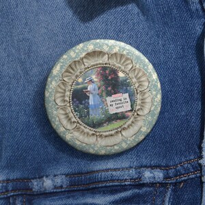 May include: A round, light blue button with a floral design border. The center features a vintage image of a person reading in a garden, with the text "reading is my favorite sport".