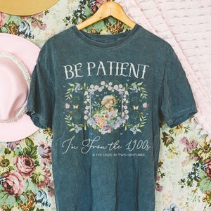 May include: A dark blue t-shirt with a floral design and the text "BE PATIENT I'm From the 1900s & I've Lived in Two Centuries".