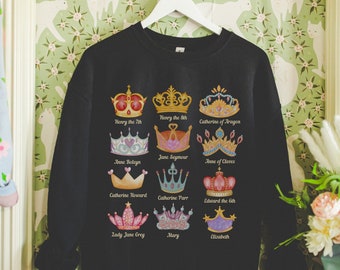 May include: Black sweatshirt with a colorful graphic of crowns and names of historical figures, including Henry the VIII, Catherine of Aragon, Jane Seymour, Anne Boleyn, Anne of Cleves, Catherine Howard, Catherine Parr, Edward the VI, Lady Jane Grey, Mary, and Elizabeth.
