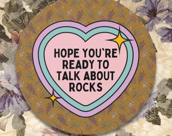 May include: A round sticker with a brown floral pattern. A pink heart with a blue and white outline contains the text "HOPE YOU'RE READY TO TALK ABOUT ROCKS".