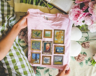 Puede incluir: Camiseta rosa con un collage de nueve cuadros enmarcados de Vincent van Gogh. Las pinturas incluyen girasoles, iris, noches estrelladas y autorretratos. La camiseta tiene el nombre y la firma del artista impresos en la parte inferior.