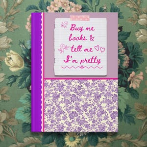May include: A decorative journal with a purple spine and a lavender cover. The cover features a floral pattern and a lined paper design with the text "Buy me books & tell me I'm pretty" in pink script.