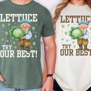 May include: Two t-shirts, one green and one white, featuring a whimsical graphic. The graphic depicts a smiling gnome holding a large head of lettuce, with the words "LETUCE TRY OUR BEST!" in bold, white letters.
