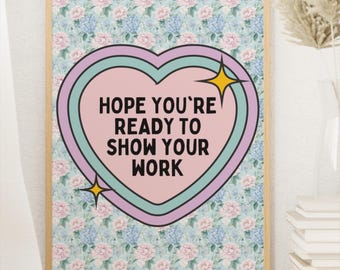 May include: A framed print with a floral background and a heart-shaped graphic. The heart contains the text "HOPE YOU'RE READY TO SHOW YOUR WORK" in a bold font. The frame is light brown.