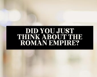 Könnte beinhalten: Ein schwarzer rechteckiger Aufkleber mit weißem Text: „DID YOU JUST THINK ABOUT THE ROMAN EMPIRE?“ Der Text ist zentriert und in einer fetten, serifenlosen Schriftart. Der Hintergrund ist verschwommen.