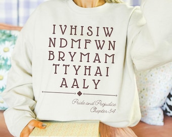 Puede incluir: Una sudadera de color crema con un gráfico marrón que dice "IVHISIW NDMFWN BRYMAM TTYHAI AALY" y "Orgullo y prejuicio Capítulo 34".