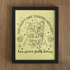 May include: A yellow framed print with a black and white illustration of a cat wearing a bow tie. The text reads "You don't like talking history? How purrr-fectly boring."