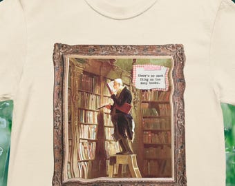 May include: Off-white t-shirt with a framed image of a man in a library, reading a book. The image includes bookshelves and the text "there's no such thing as too many books."