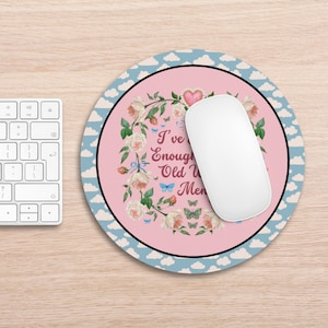 Pode incluir: Um tapete de rato redondo rosa com uma borda azul e um padrão de nuvens brancas. O centro do tapete de rato apresenta uma coroa de rosas brancas e borboletas azuis com o texto "Já tive o suficiente de homens velhos".