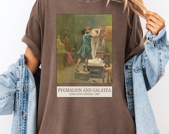 Può includere: T-shirt marrone con il dipinto "Pygmalion e Galatea" di Jean-Léon Gérôme, 1890. L'opera raffigura un uomo che abbraccia una statua di donna. La maglietta ha maniche arrotolate e girocollo.