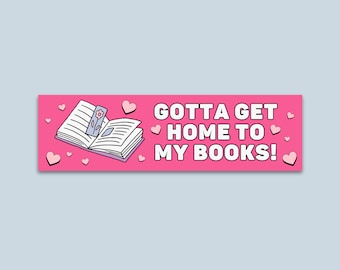 May include: A pink bumper sticker with the text "GOTTA GET HOME TO MY BOOKS!" in white. The sticker features an open book with a floral bookmark and pink hearts scattered around the text and book.