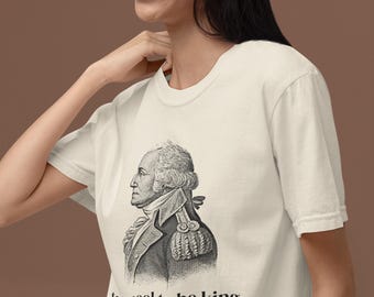 May include: Cream-colored t-shirt featuring a black and white illustration of a historical figure, with the text "too cool to be king" in a black, sans-serif font. The shirt has short sleeves and a crew neck.