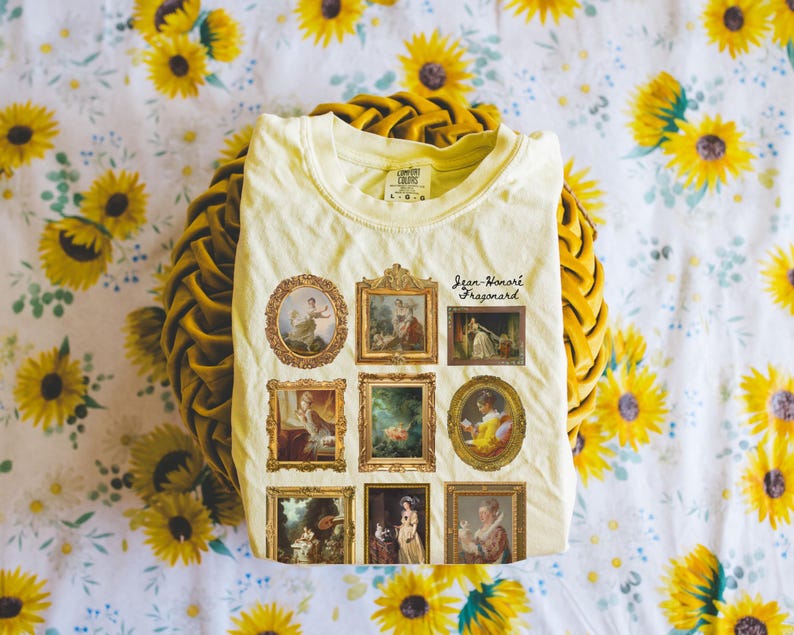 May include: A light yellow t-shirt featuring a print of nine framed paintings. The paintings are all in a similar style and depict people in various poses. The text "Jean-Honor&eacute; Fragonard" is printed below the paintings.