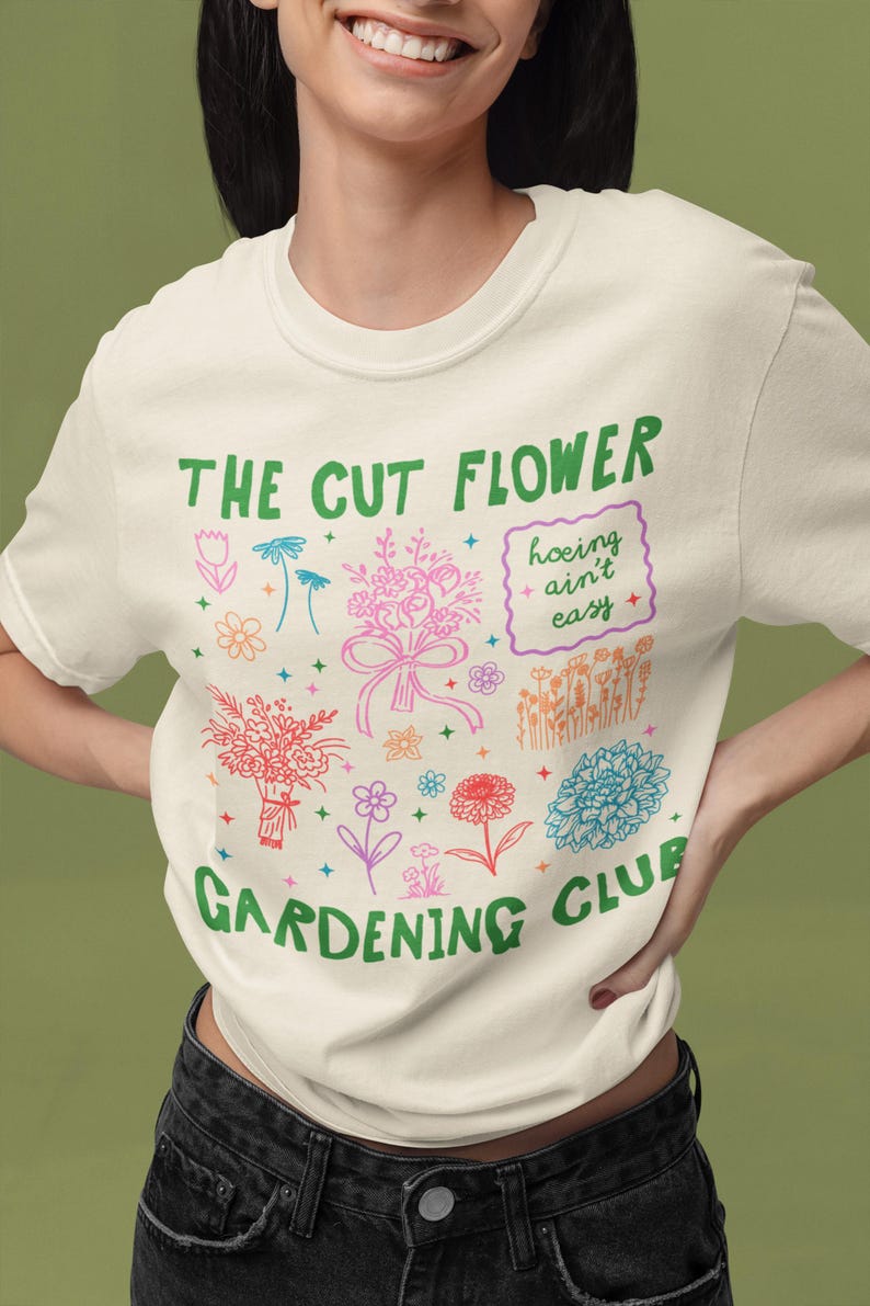 K&ouml;nnte beinhalten: Ein wei&szlig;es T-Shirt mit einer gr&uuml;nen Grafik, auf der "The Cut Flower Gardening Club" steht und ein Blumenstrau&szlig;, ein Blumentopf und der Text "hoeing ain't easy" abgebildet sind.
