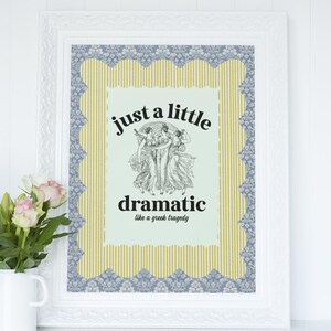 May include: White framed art print with the text "just a little dramatic like a greek tragedy". The print has a light green background with a black and white illustration of three figures. The frame has a blue and yellow patterned border.