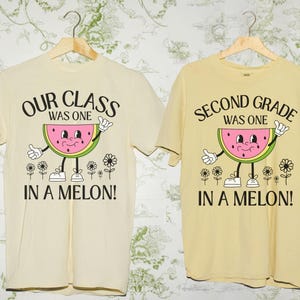 Puede incluir: Dos camisetas de manga corta, una crema y otra amarilla, con un gráfico de sandía. La camiseta crema dice "OUR CLASS WAS ONE IN A MELON!". La camiseta amarilla dice "SECOND GRADE WAS ONE IN A MELON!"