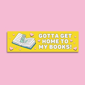 May include: A yellow banner with the text "GOTTA GET HOME TO MY BOOKS!" in white. A cartoon image of an open book with a bookmark is on the left side of the banner. There are pink hearts scattered around the banner.