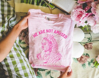 May include: Pink t-shirt with a pink graphic of Queen Victoria with the text "We are not amused, but we do love some historical tea."