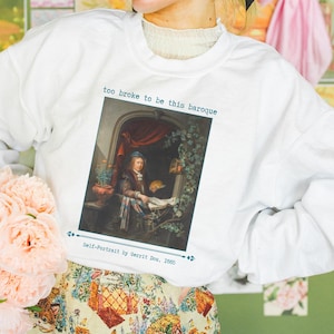 Op de afbeelding: Witte sweatshirt met een ingelijste afbeelding van een schilderij met de tekst "too broke to be this baroque" erboven. Het schilderij is een zelfportret van Gerrit Dou, 1665. De persoon draagt een bloemenrok en houdt een boeket roze bloemen vast.