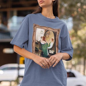 May include: A blue t-shirt with a vintage-style painting of two women in a room with a mirror. The text on the mirror reads "If it's moody, give me candy".