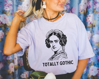 May include: A light purple t-shirt with a black and white illustration of a woman with a lace cap and the text "TOTALLY GOTHIC".