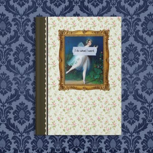 May include: A white journal with a floral pattern and a gold frame containing a picture of a woman in a white dress dancing in a garden. The text "I do what I want" is on a blue banner in the picture.