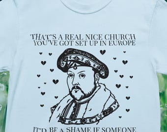 Könnte beinhalten: Hellblaues T-Shirt mit einer schwarzen Grafik von König Heinrich VIII. und dem Text "THAT'S A REAL NICE CHURCH YOU'VE GOT SET UP IN EUROPE" und "IT'D BE A SHAME IF SOMEONE WANTED A DIVORCE". Enthält den Text "KING HENRY VIII, PROBABLY 1527".