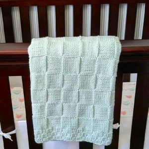 May include: A light green knitted baby blanket with a checkered pattern. The blanket is draped over a crib.
