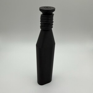 Puede incluir: Un tap&oacute;n de botella negro con un cuello cil&iacute;ndrico y una parte superior plana y cuadrada. El cuello presenta una serie de crestas circulares. El tap&oacute;n tiene un dise&ntilde;o geom&eacute;trico y moderno. El tap&oacute;n est&aacute; hecho de un material oscuro y s&oacute;lido.
