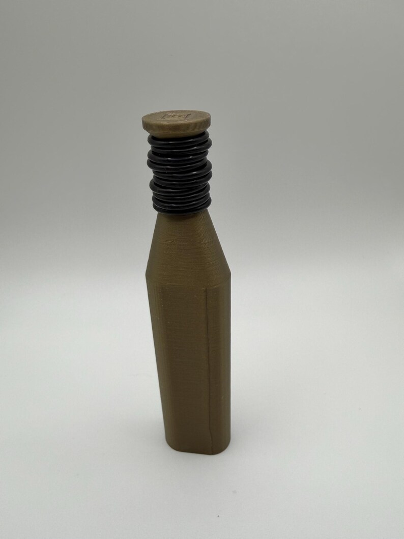 Puede incluir: Una botella marr&oacute;n con un cuello negro y acanalado y una parte superior plana y circular. La botella tiene forma rectangular con lados angulados. La parte superior de la botella tiene un peque&ntilde;o dise&ntilde;o cuadrado.