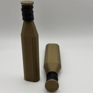 May include: Two brown bottle stoppers with black rubber rings and a square top. One stopper is upright, the other is lying on its side. The stoppers have a geometric design and are made of a solid material.