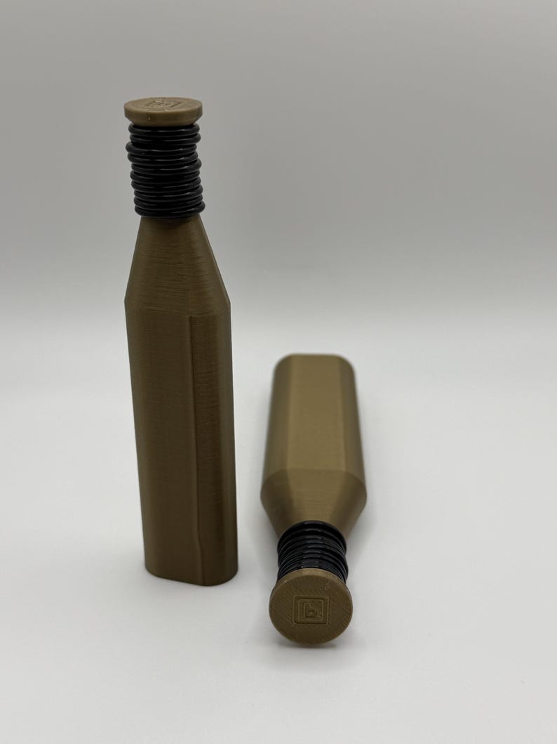 May include: Two brown bottle stoppers with black rubber rings and a square top. One stopper is upright, the other is lying on its side. The stoppers have a geometric design and are made of a solid material.