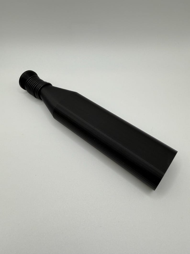 May include: A black bottle stopper with a ribbed neck and a long, rectangular body. The stopper is made of a solid, opaque material and is designed to fit into a bottle opening. The design is simple and modern.