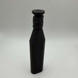 May include: A black bottle stopper with a cylindrical neck and a flat, round top. The neck features a series of horizontal ridges. The top has a square design in the center. The bottle stopper is made of a solid, matte black material.