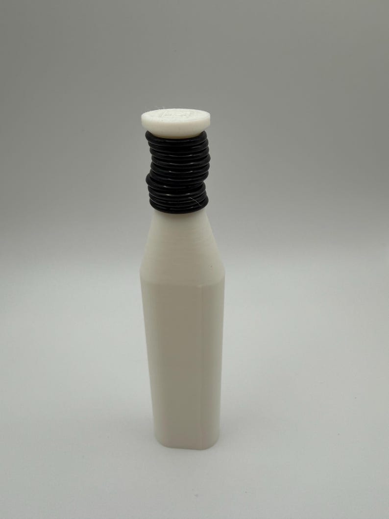 Puede incluir: Una botella blanca con un cuello negro enrollado y una tapa blanca. La botella tiene una base rectangular y un cuerpo ligeramente c&oacute;nico. La tapa parece tener un dise&ntilde;o circular. El fondo es de color neutro.