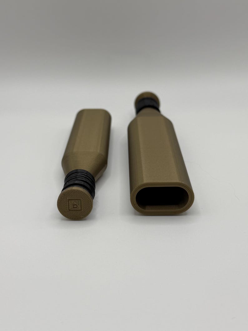 May include: Two brown bottle stoppers with black rubber seals. One stopper is inserted into a bottle, and the other is separate. The stoppers have a geometric design and a small square logo on the top. The background is plain white.