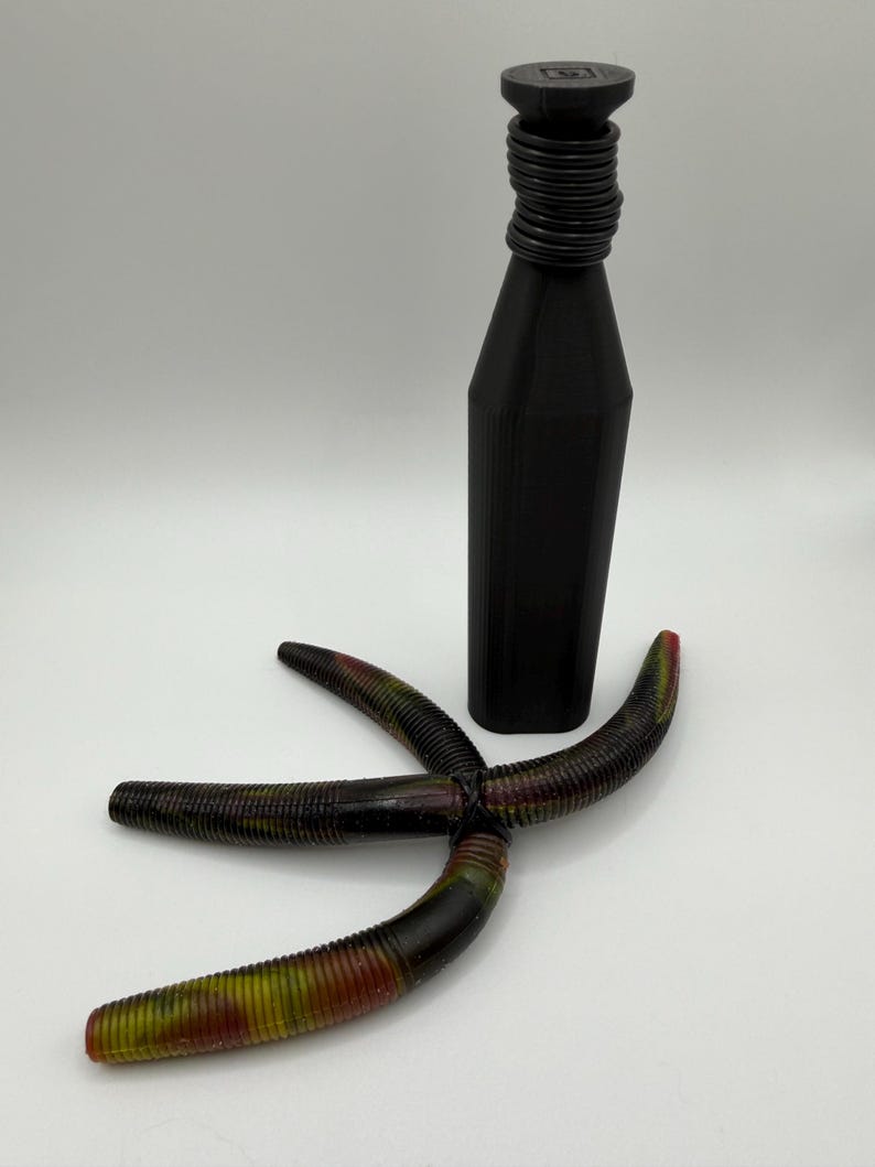 May include: A black bottle stopper with a ridged neck and a four-armed, multi-colored fishing lure. The lure is primarily black with red, yellow, and green accents. The bottle stopper is approximately 6 inches tall.