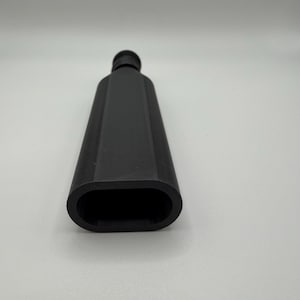 Puede incluir: Una botella negra rectangular con una abertura ovalada redondeada. La botella tiene un cuello estrecho y un acabado liso y mate. El objeto est&aacute; sobre un fondo blanco.